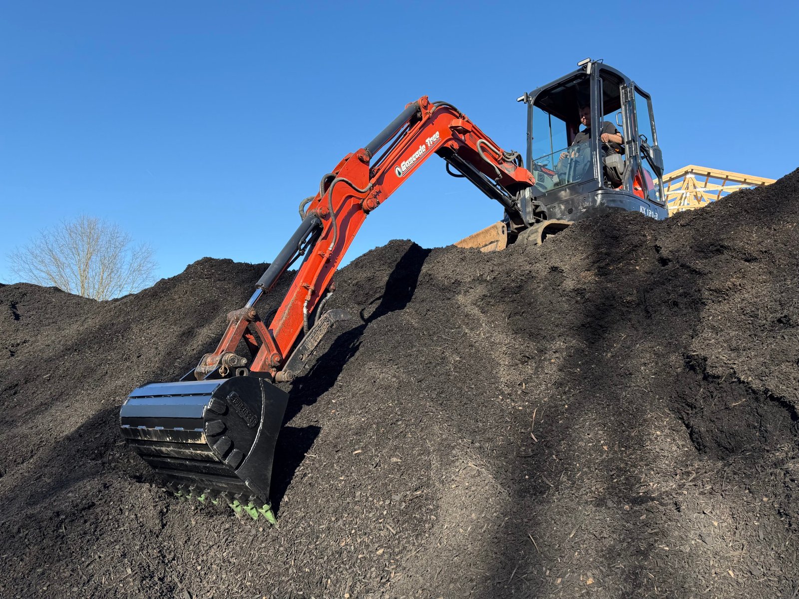 Kubota excavator working in a mulch pile with a custom bucket